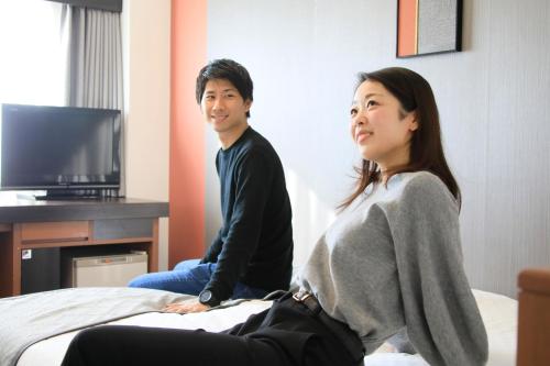 a man and a woman sitting on a bed at Richmond Hotel Higashi Osaka in Osaka