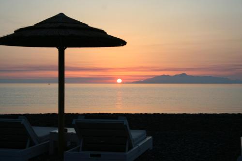 an umbrella and chairs on a beach with the sunset at Arion Bay Hotel Santorini in Kamari