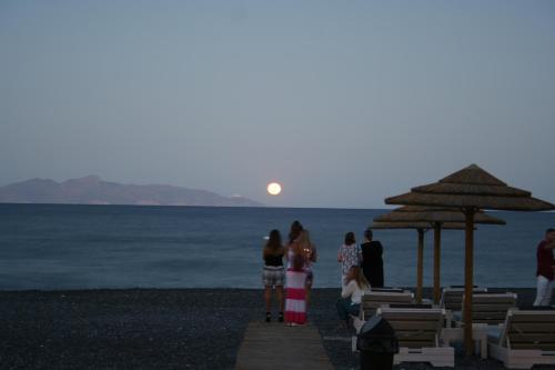 a group of people standing on a beach with the moon in the sky at Arion Bay Hotel Santorini in Kamari
