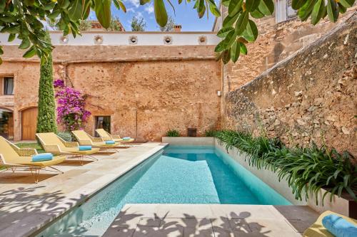 a swimming pool with chairs and a brick wall at Sa Creu Nova Petit Palais Art & Spa in Campos