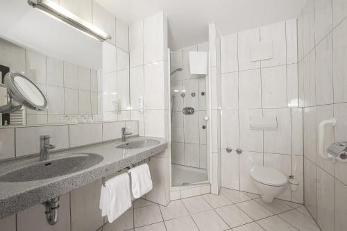 a bathroom with two sinks and a toilet and a shower at Johannesbad Hotel Königshof in Bad Füssing