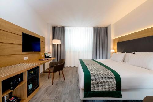ナポリにあるホリデイ イン ネープルスのベッド、デスク、テレビが備わるホテルルームです。