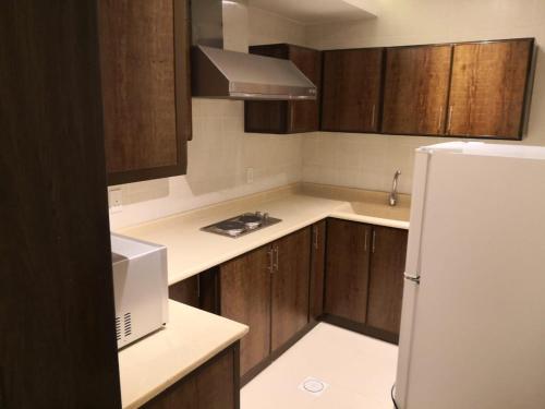 アル・コバールにあるMJ Apartmentsの木製のキャビネットと白い冷蔵庫を備えたキッチン