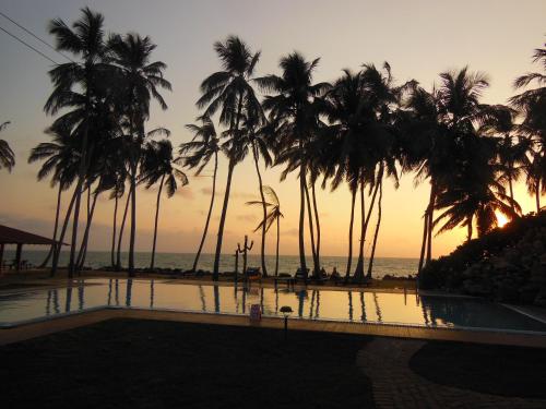 a pool with palm trees and the ocean at sunset at Sanmali Beach Hotel in Marawila