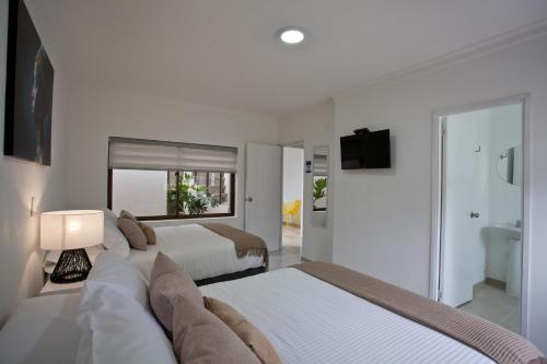 a white bedroom with two beds and a bathroom at Mucura Hotel & Spa in Cartagena de Indias