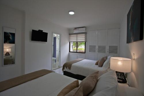 a white bedroom with two beds and a tv at Mucura Hotel & Spa in Cartagena de Indias