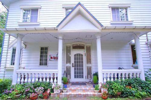 a white house with a porch with potted plants at Mt Fuji B&B PENSION LE LAGON in Yamanakako