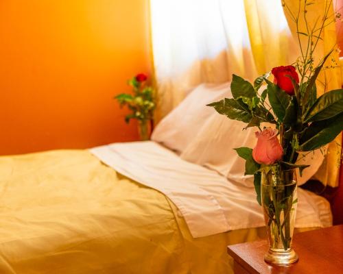 a vase with roses on a table next to a bed at Peru Quechua's Lodge Ollantaytambo in Ollantaytambo