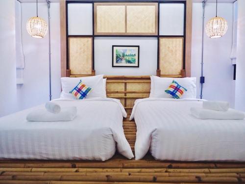 two beds in a room with white sheets and windows at Luck Esan Loft in Ubon Ratchathani