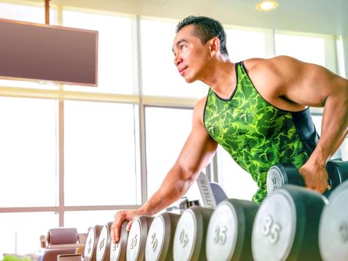 a man in a green shirt standing over a row of weights at Novotel Abu Dhabi Gate in Abu Dhabi