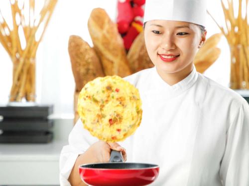 a woman chef holding a pizza in a bowl at Novotel Abu Dhabi Gate in Abu Dhabi