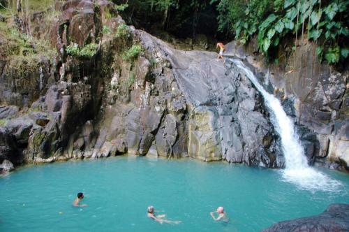 three people swimming in a pool in front of a waterfall at Ô Fil de l'Eau in Pointe-Noire