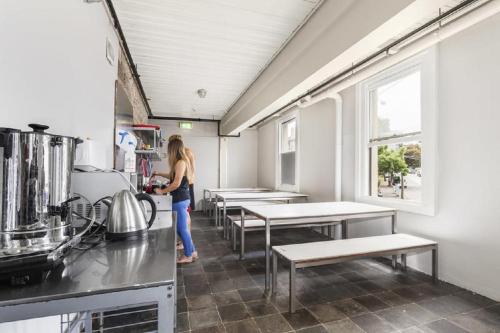 a woman standing in a kitchen with tables and benches at Summer House Melbourne in Melbourne