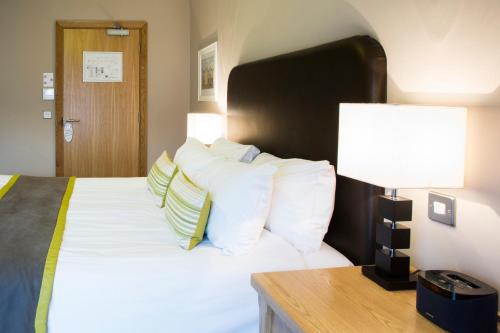 a bedroom with a bed with white pillows and a lamp at Breckland Lodge in Attleborough