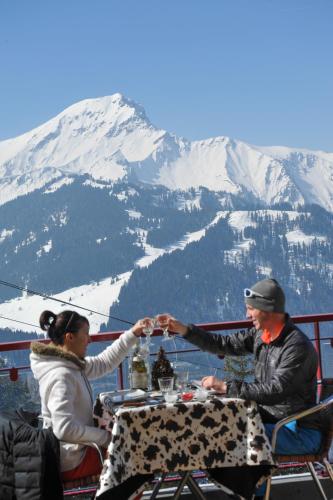 a man and woman sitting at a table in front of a mountain at L'Escale (accès en télécabine) in Châtel