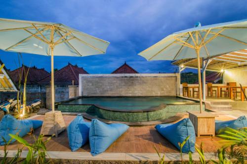 a swimming pool with two umbrellas and blue pillows at D'Yuki Huts Lembongan in Nusa Lembongan