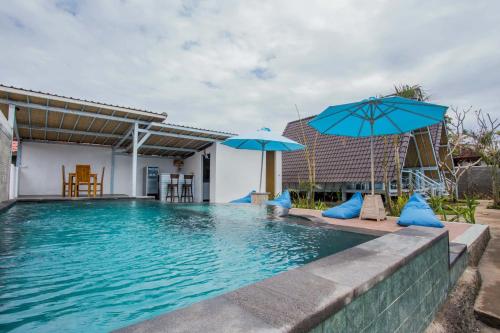 a swimming pool with two blue umbrellas at D'Yuki Huts Lembongan in Nusa Lembongan