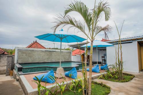 a pool with blue umbrellas and chairs and a palm tree at D'Yuki Huts Lembongan in Nusa Lembongan