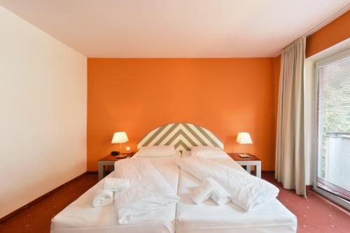a white bed in a room with an orange wall at Hotel Neutor Express in Salzburg