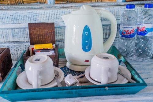 a tray with a tea pot and cups and water bottles at D'Yuki Huts Lembongan in Nusa Lembongan
