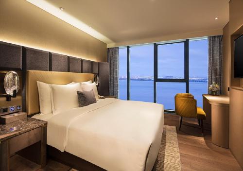 a bedroom with a bed and a desk and a large window at Grand Bay Hotel Zhuhai in Zhuhai
