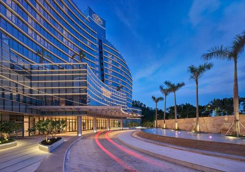 a large building with palm trees in front of a road at Grand Bay Hotel Zhuhai in Zhuhai