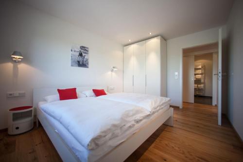 a white bedroom with a large white bed with red pillows at Chalet Alpenrose 134qm am Golfplatz Oberstaufen in Oberstaufen