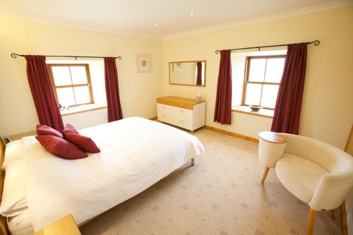 a bedroom with a bed and a chair and two windows at Sebay Mill Holiday Apartments in Toab