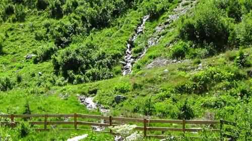 a hillside with a fence and a creek at Haus Bergheim in Sankt Leonhard im Pitztal