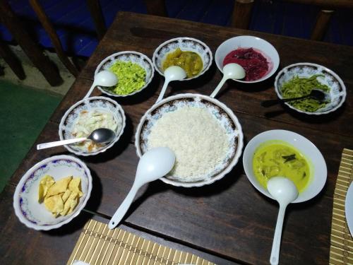 a wooden table topped with bowls of food and spoons at Apurvi Homestay in Ella