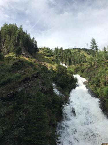 a river in a field next to a hill with trees at Berghaus Außergschlöß in Matrei in Osttirol