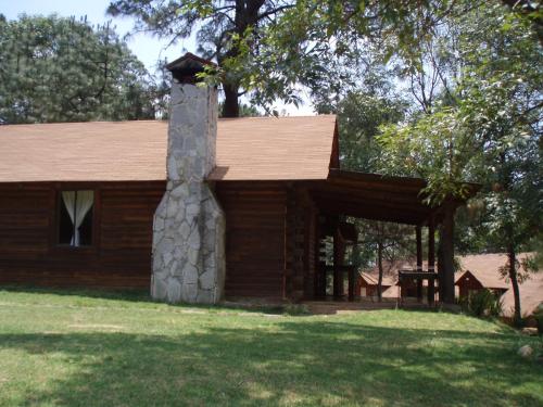 a log cabin with a stone chimney in the yard at Sierra Paraiso Hotel in Mazamitla