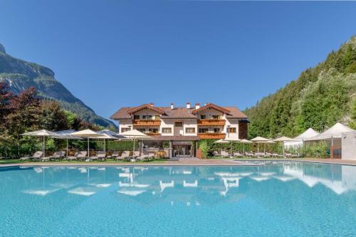a resort with a large swimming pool in front of a mountain at Hotel La Maison Wellness & Spa in Alleghe