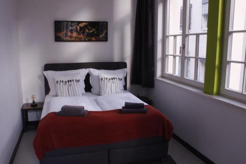 a bedroom with a bed with a red blanket and two windows at Silentio Apartments in Leipzig