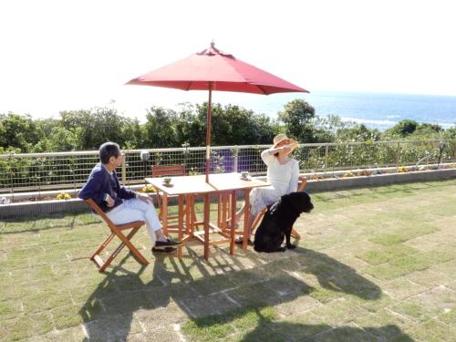 two people and a dog sitting at a table with an umbrella at Sol e Mar in Tatsugo