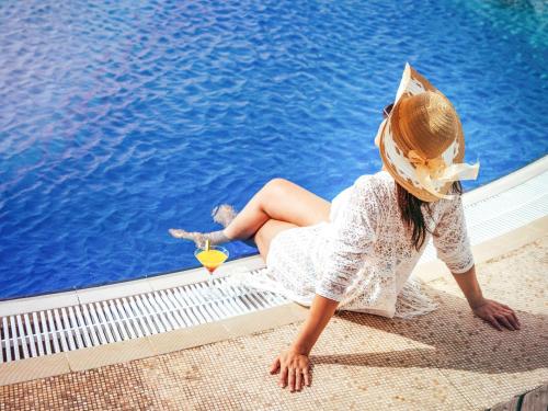 a young girl wearing a hat sitting next to a pool at Novotel Abu Dhabi Gate in Abu Dhabi