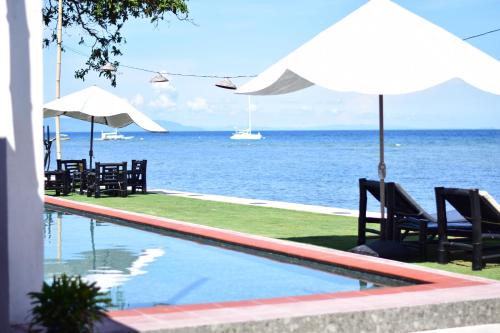 a swimming pool with chairs and umbrellas and the ocean at the beachhouse in Dalaguete