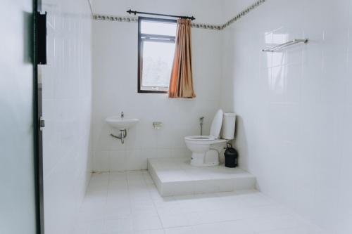 a white bathroom with a toilet and a sink at Candra Cottage in Munduk