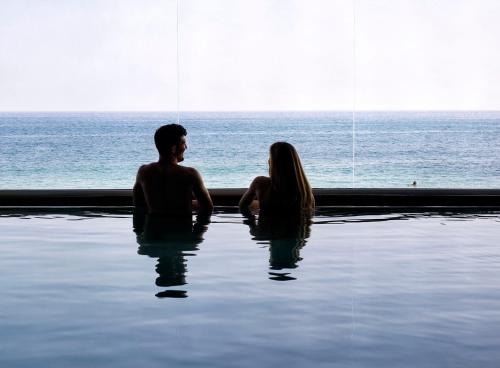 a man and woman sitting in a swimming pool near the ocean at White Bay in Fontane Bianche