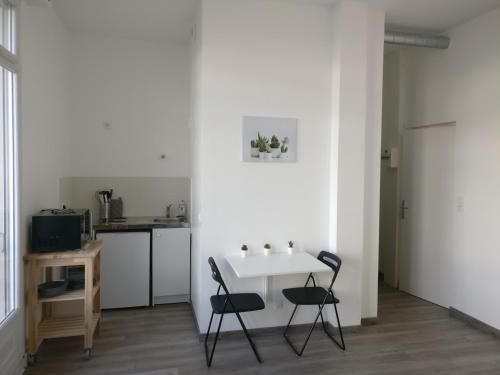 eine weiße Küche mit einem Tisch und 2 Stühlen in der Unterkunft Appart Hôtel L'Angélique in Saint-Nazaire