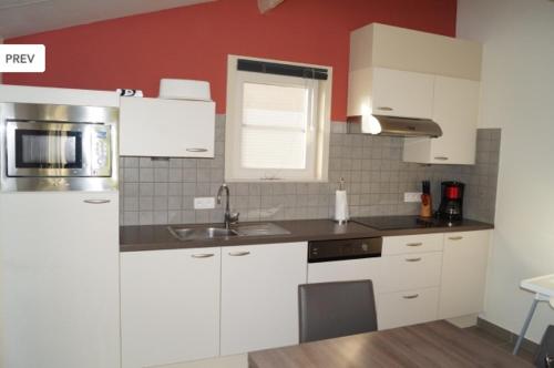 a kitchen with white cabinets and a red wall at Zee en polder nummer 16 in Middelkerke