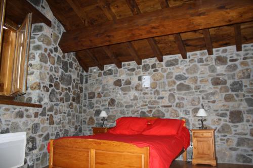 um quarto com uma cama vermelha numa parede de pedra em la forge d'andribet em Axiat