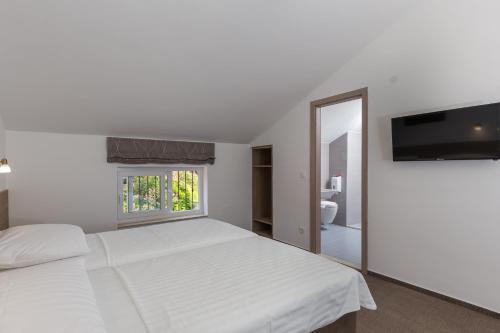 a white bedroom with a bed and a flat screen tv at Hotel Vimbula - Komolac in Mokošica
