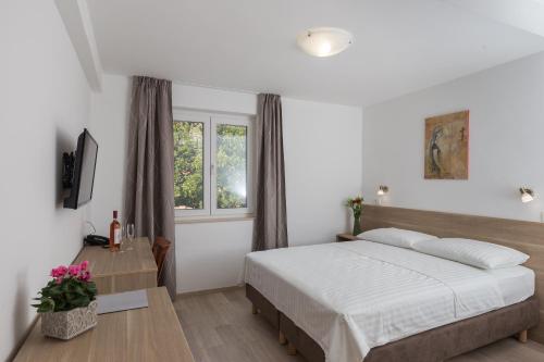 a white bedroom with a bed and a window at Hotel Vimbula - Komolac in Mokošica