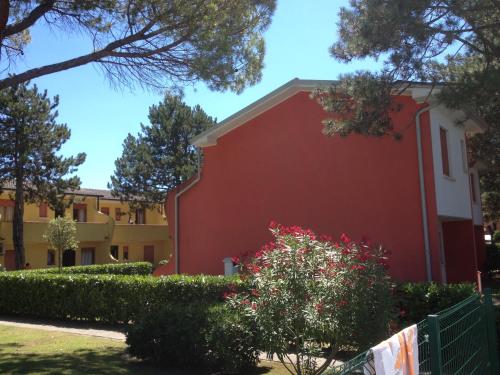 a red building with a fence and a bush at Adriella apartments in Bibione