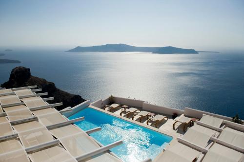 uitzicht op een zwembad met stoelen en de oceaan bij Gold Suites - Small Luxury Hotels of the World in Imerovígli