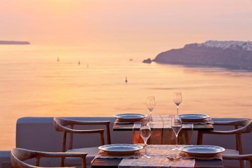 a table with glasses and plates on top of the ocean at Gold Suites - Small Luxury Hotels of the World in Imerovigli