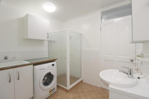 een witte badkamer met een wasmachine en een wastafel bij Beachfront 4, 25 Willow Street in Crescent Head