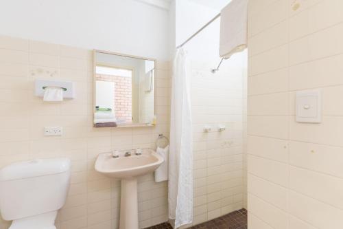 Baño blanco con aseo y lavamanos en Aquajet Motel, en Coffs Harbour