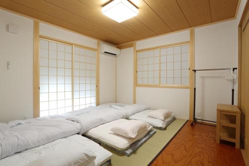 a room with a row of beds in a room with windows at Guest House Keiten in Kyoto